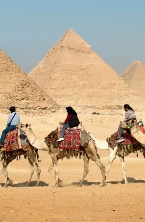 Tourists riding camels near the Great Pyramids of Giza, Egypt under clear skies.